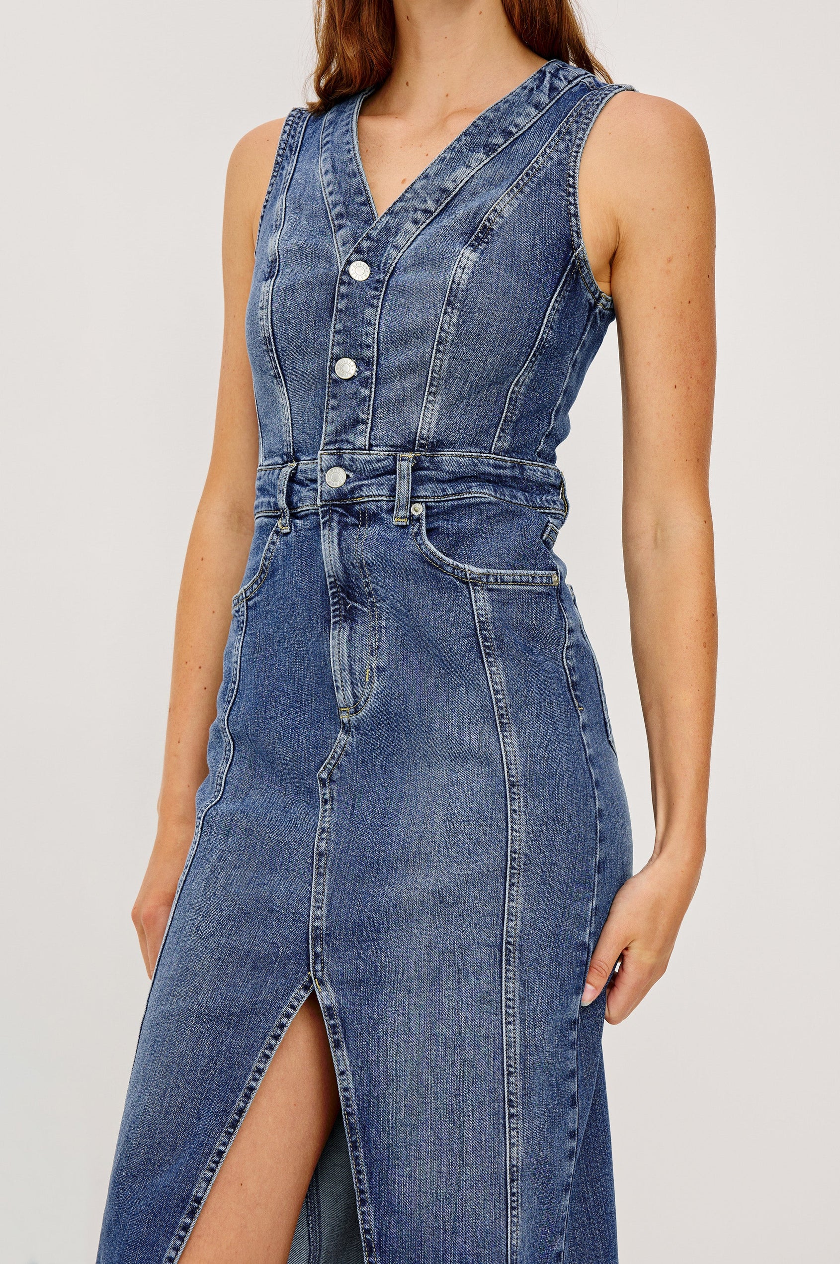 Westwood Sleeveless Denim Midi Dress with Belt Loops, a Button and Zipper Closure for the Skirt and Button Closure on the Bodice, a V neck, a Front Center Thigh Slit, Two Front Pockets  and Two Back Patch Pockets in Forget Me Not Colorway, a Blue - Close Up Front View Featured on Model