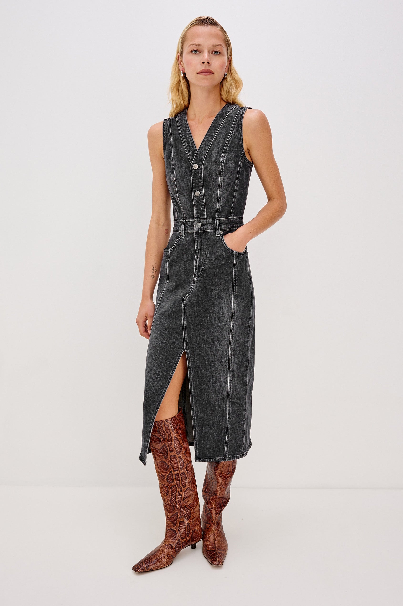 Westwood Sleeveless Denim Midi Dress with Belt Loops, a Button and Zipper Closure for the Skirt and Button Closure on the Bodice, a V neck, a Front Center Thigh Slit, Two Front Pockets  and Two Back Patch Pockets in Black Pearl Colorway, a washed black- Front Full Body View Featured on Model