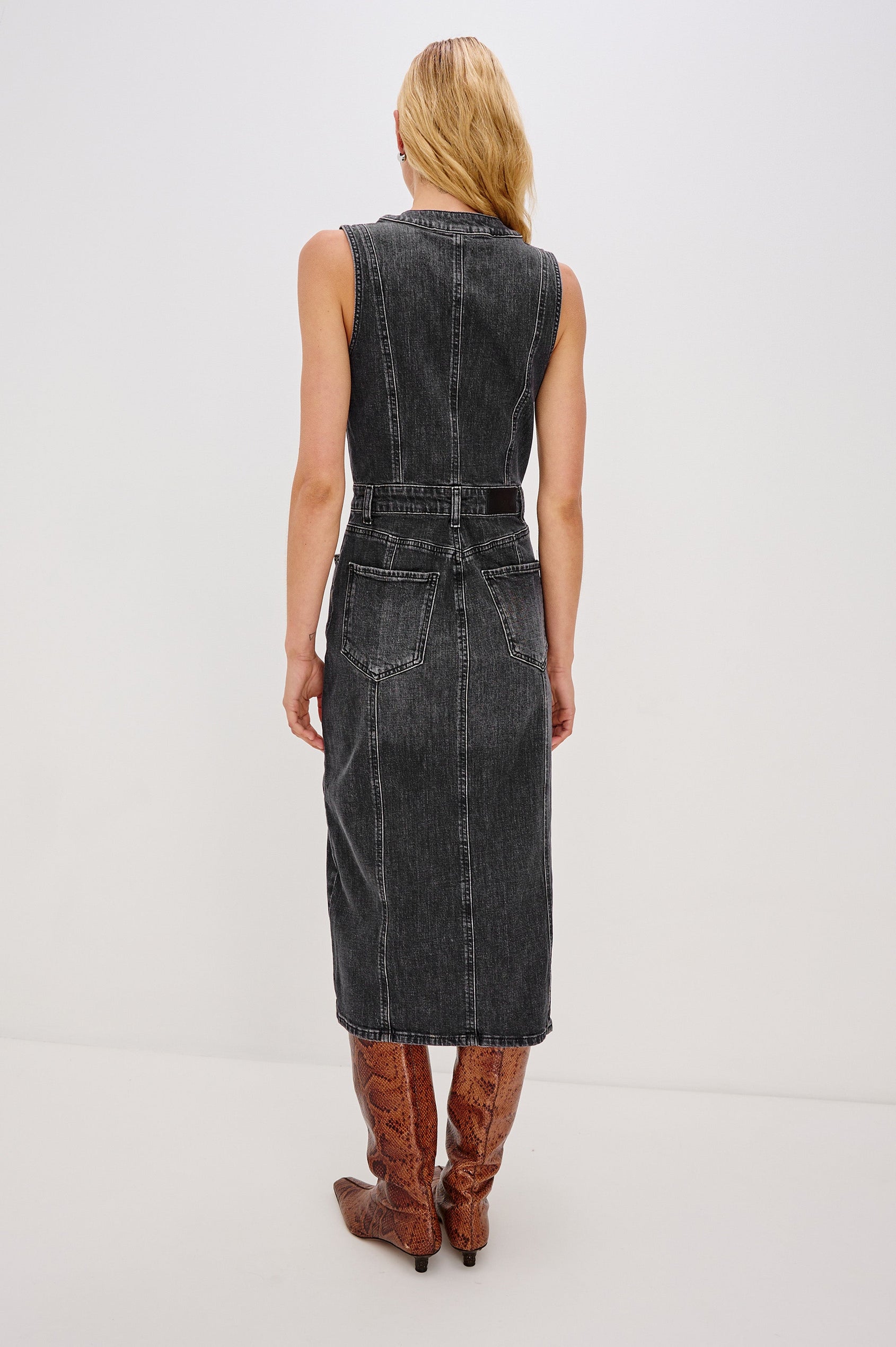 Westwood Sleeveless Denim Midi Dress with Belt Loops, a Button and Zipper Closure for the Skirt and Button Closure on the Bodice, a V neck, a Front Center Thigh Slit, Two Front Pockets  and Two Back Patch Pockets in Black Pearl Colorway, a washed black- Back Full Body View Featured on Model