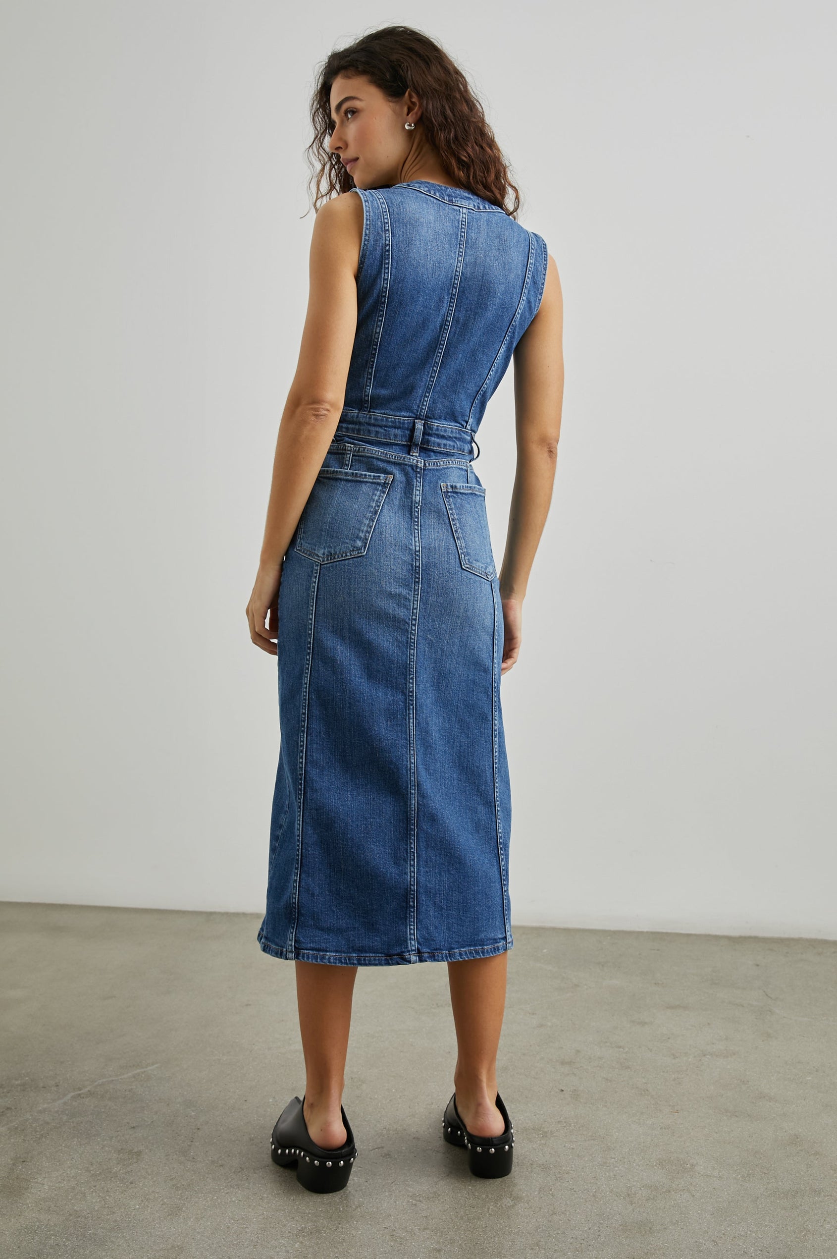 Westwood Sleeveless Denim Midi Dress with Belt Loops, a Button and Zipper Closure for the Skirt and Button Closure on the Bodice, a V neck, a Front Center Thigh Slit, Two Front Pockets  and Two Back Patch Pockets in Forget Me Not Colorway, a Blue - Back Full Body View Featured on Model