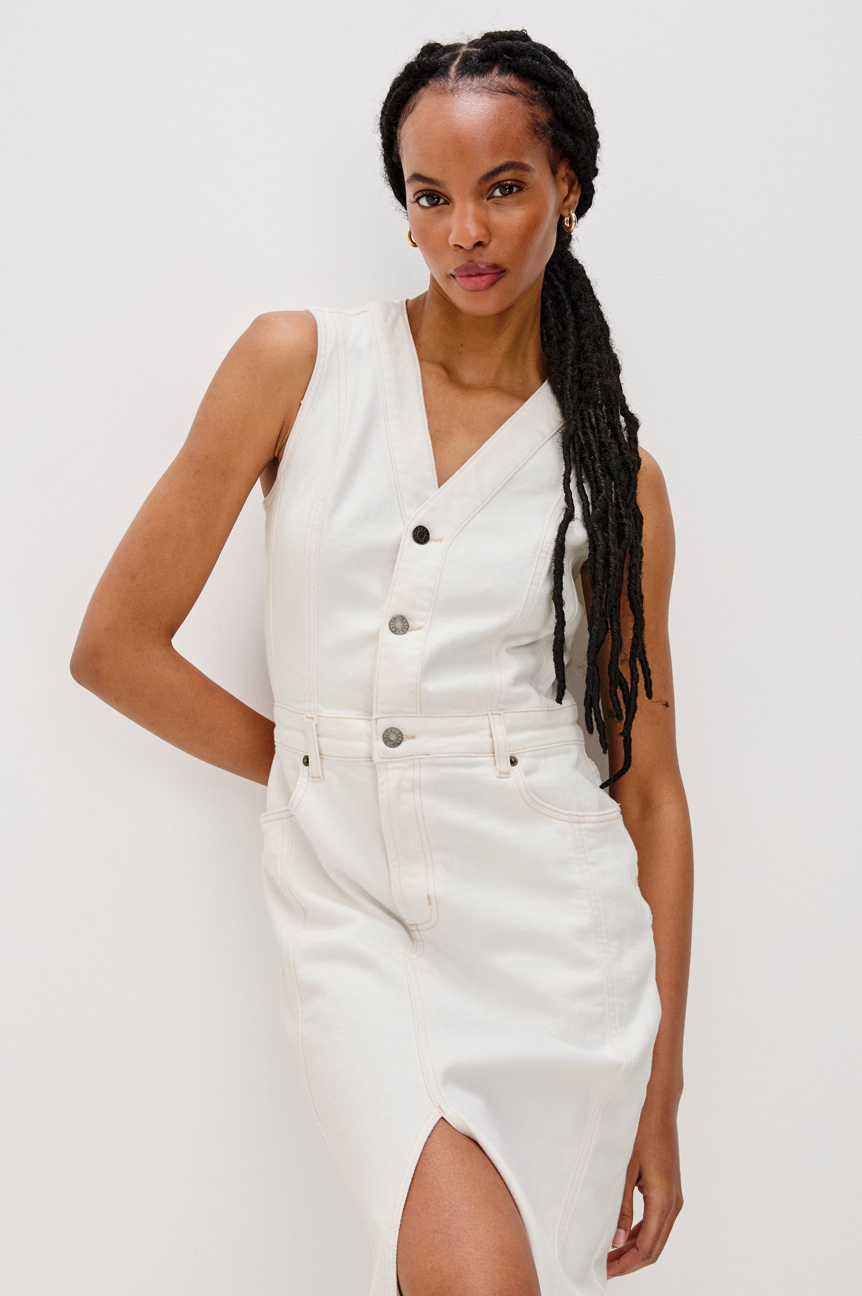 Westwood Sleeveless Denim Midi Dress with Belt Loops, a Button and Zipper Closure for the Skirt and Button Closure on the Bodice, a V neck, a Front Center Thigh Slit, Two Front Pockets  and Two Back Patch Pockets in Vintage Ecru Colorway - front view on model