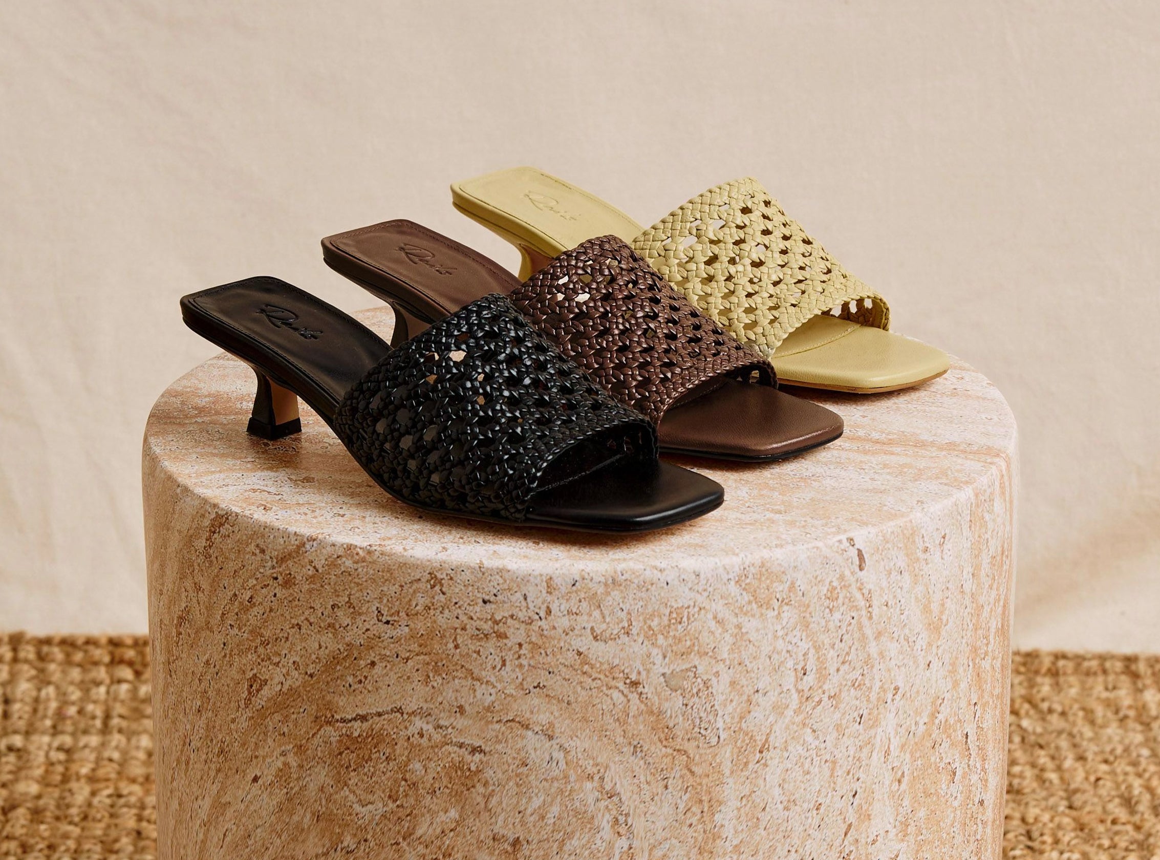 Three pairs of high-heeled shoes in black, brown, and gold on a textured surface.