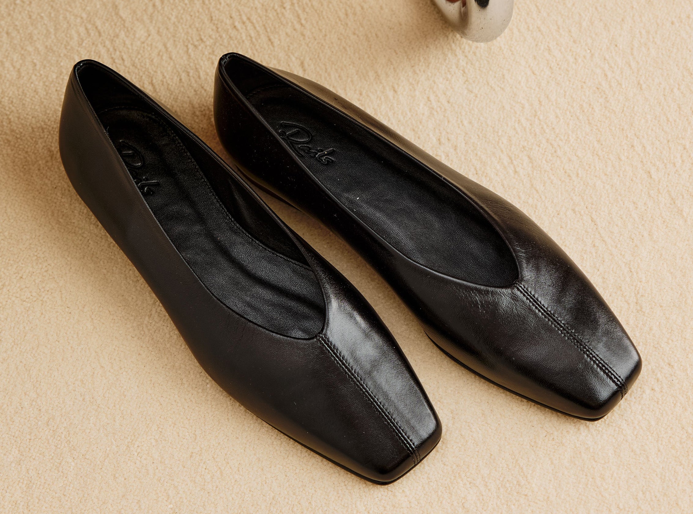 A pair of black leather ballet flats against a beige floor.