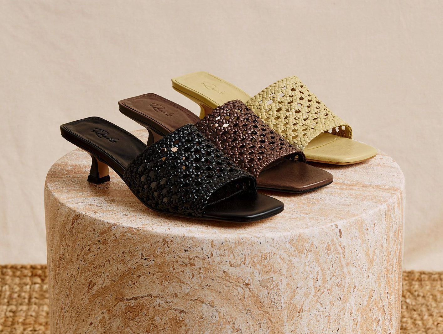 Three pairs of high-heeled shoes in black, brown, and gold on a textured surface.