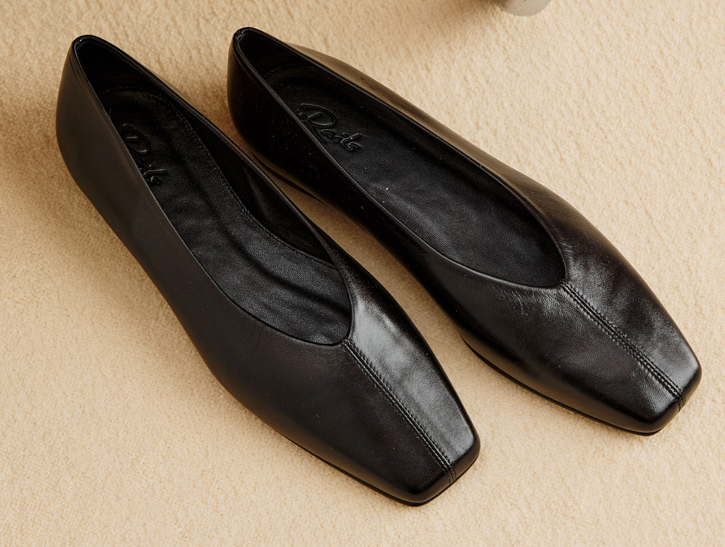 A pair of black leather ballet flats against a beige floor.