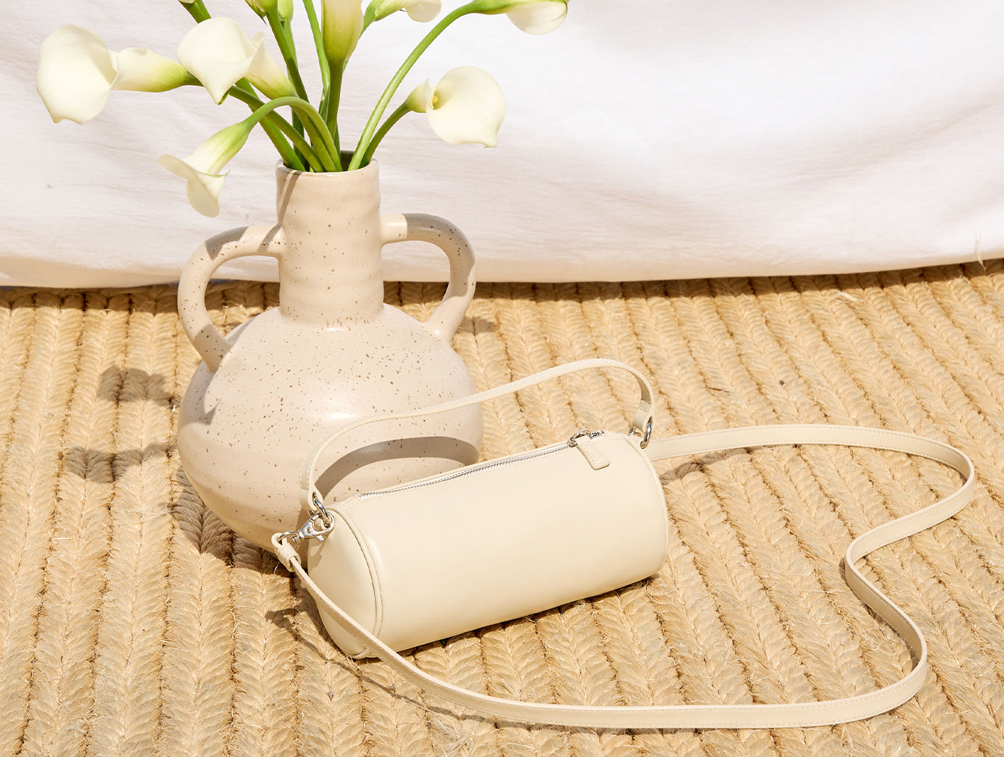 Beige handbag next to a vase with white flowers on a woven surface