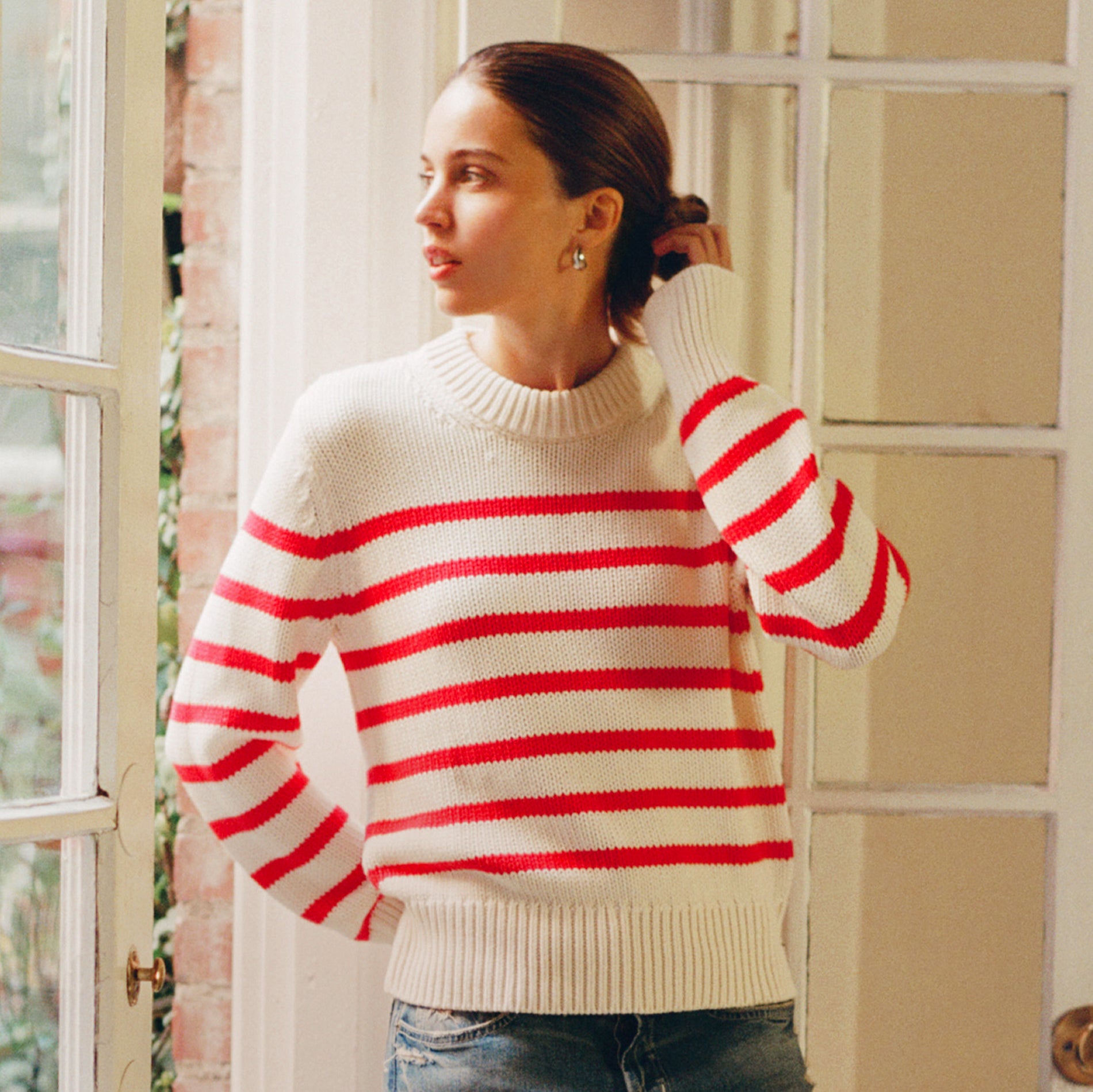 Woman wearing a white sweater with red stripes indoors.