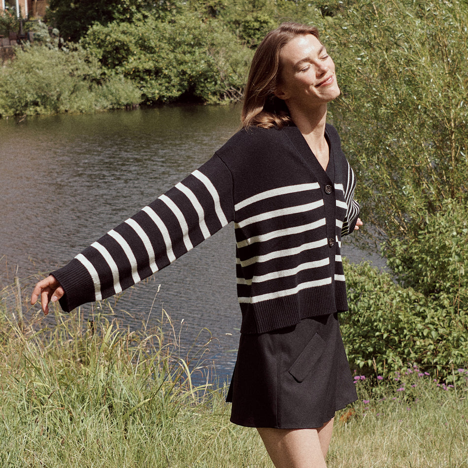 EDITORIAL IMAGE OF MODEL IN FIELD WEARING GENEVA SWEATER IN BLACK OATMEAL STRIPES