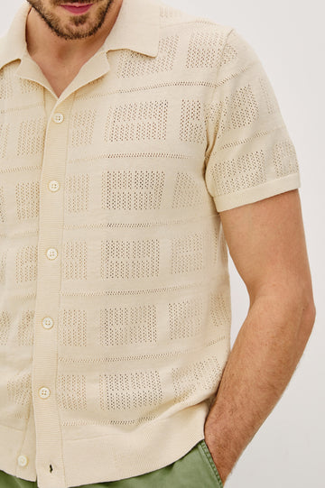 Yates Button Front Knit Shirt with Short Sleeves, a Relaxed Collar and Lapel, Ribbed Sleeve Cuff, Collar, Hem and Front Button Placket in Cream Colorway. Front Detail View Shown on Model.