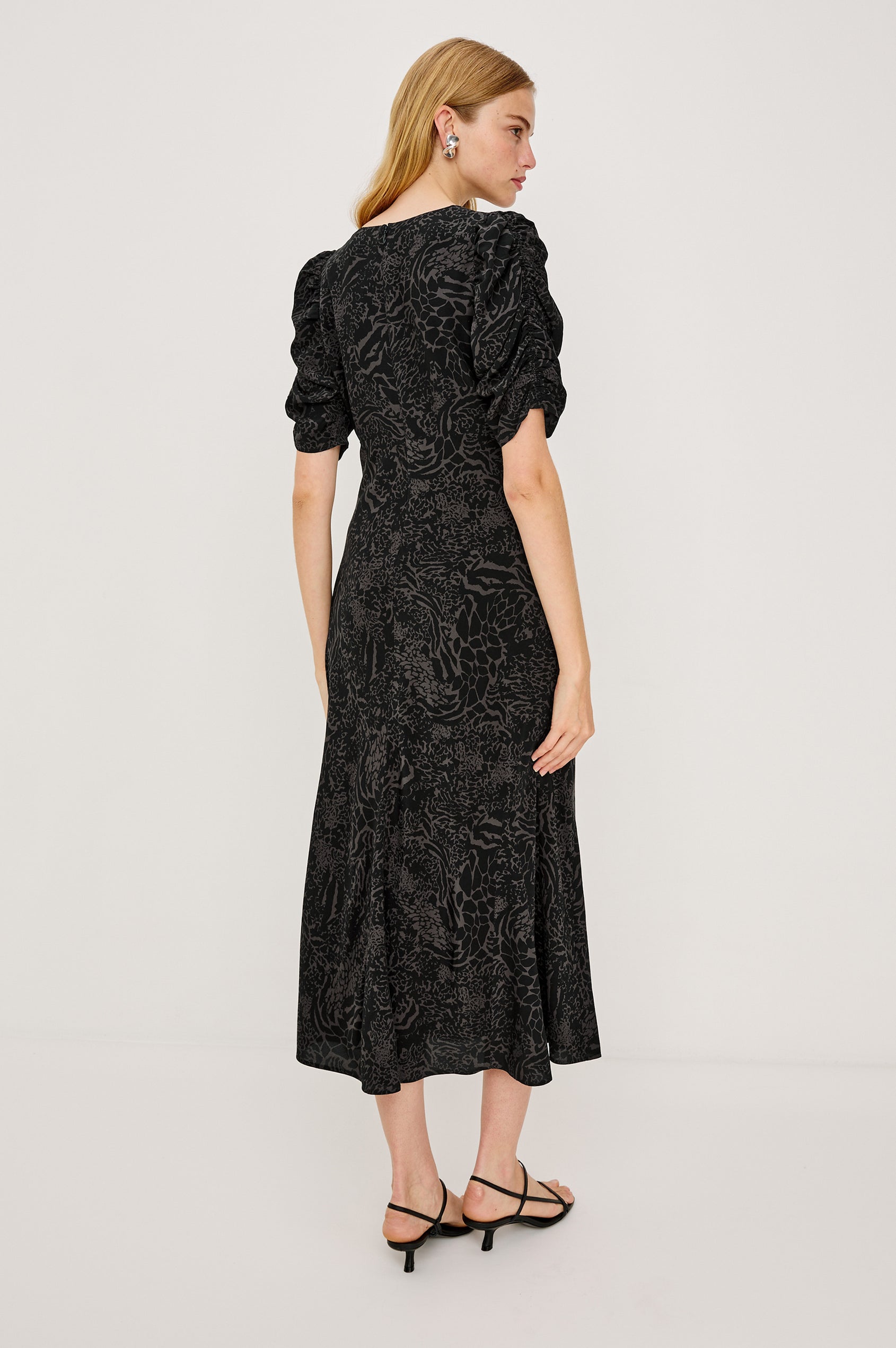 Zariah Midi Dress in Rayon Crepe With Deep V-Neckline, and Short Puff Shirred Sleeves in Charcoal Mixed Animal Print Colorway - Full Body View Featured on Model Sitting