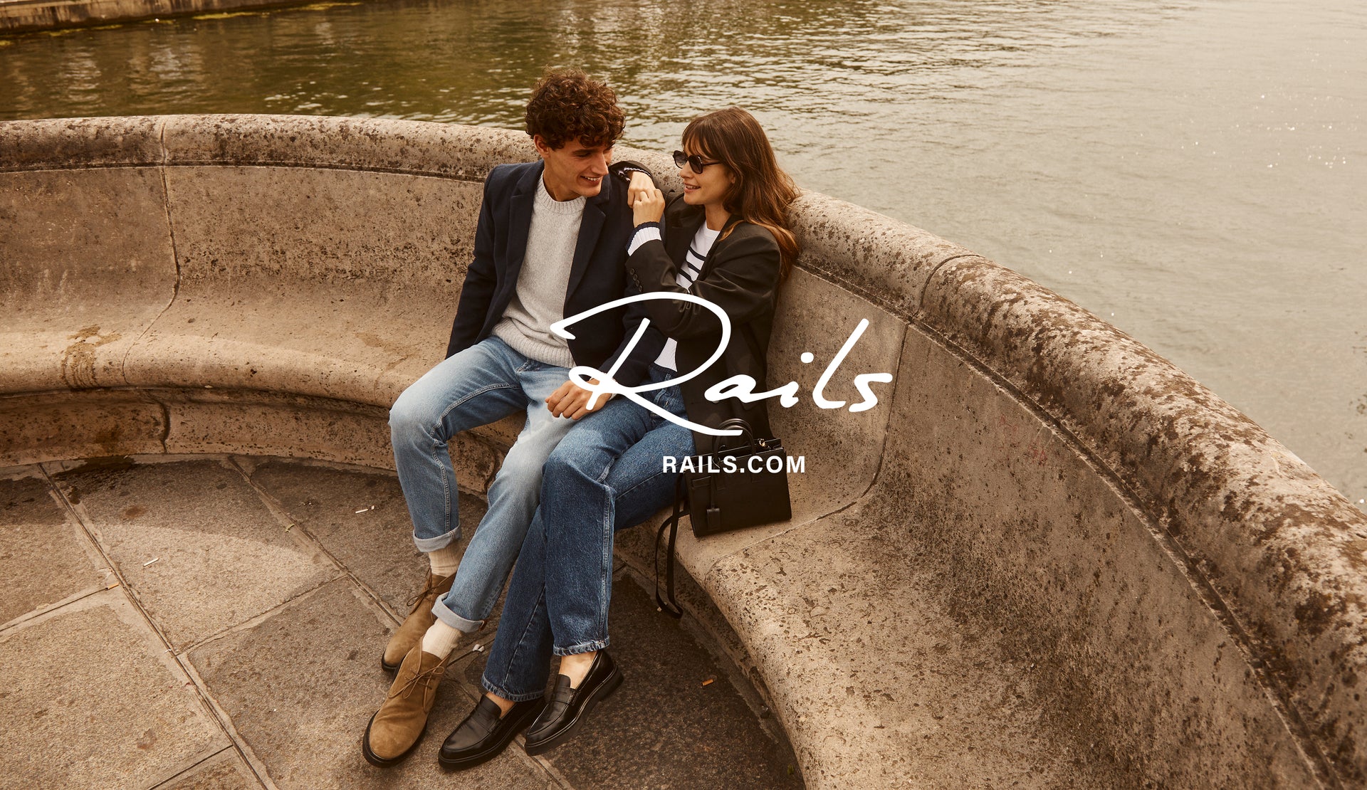 EDITORIAL IMAGE OF TWO MODELS SITTING OUTSIDE. FIRST MODEL IS WEARING LARK COAT, DONOVAN SWEATER, AND CLAYTON SLIM STRAIGHT JEANS. SECOND MODEL IS WEARING JAC BLAZER, GEMMA SWEATER, AND TOPANGA STRAIGHT JEANS. 