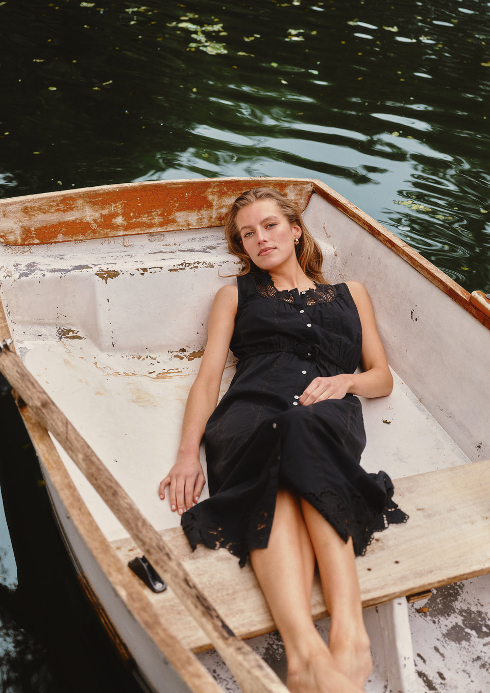 Woman in a black dress sitting in a small boat on a body of water.
