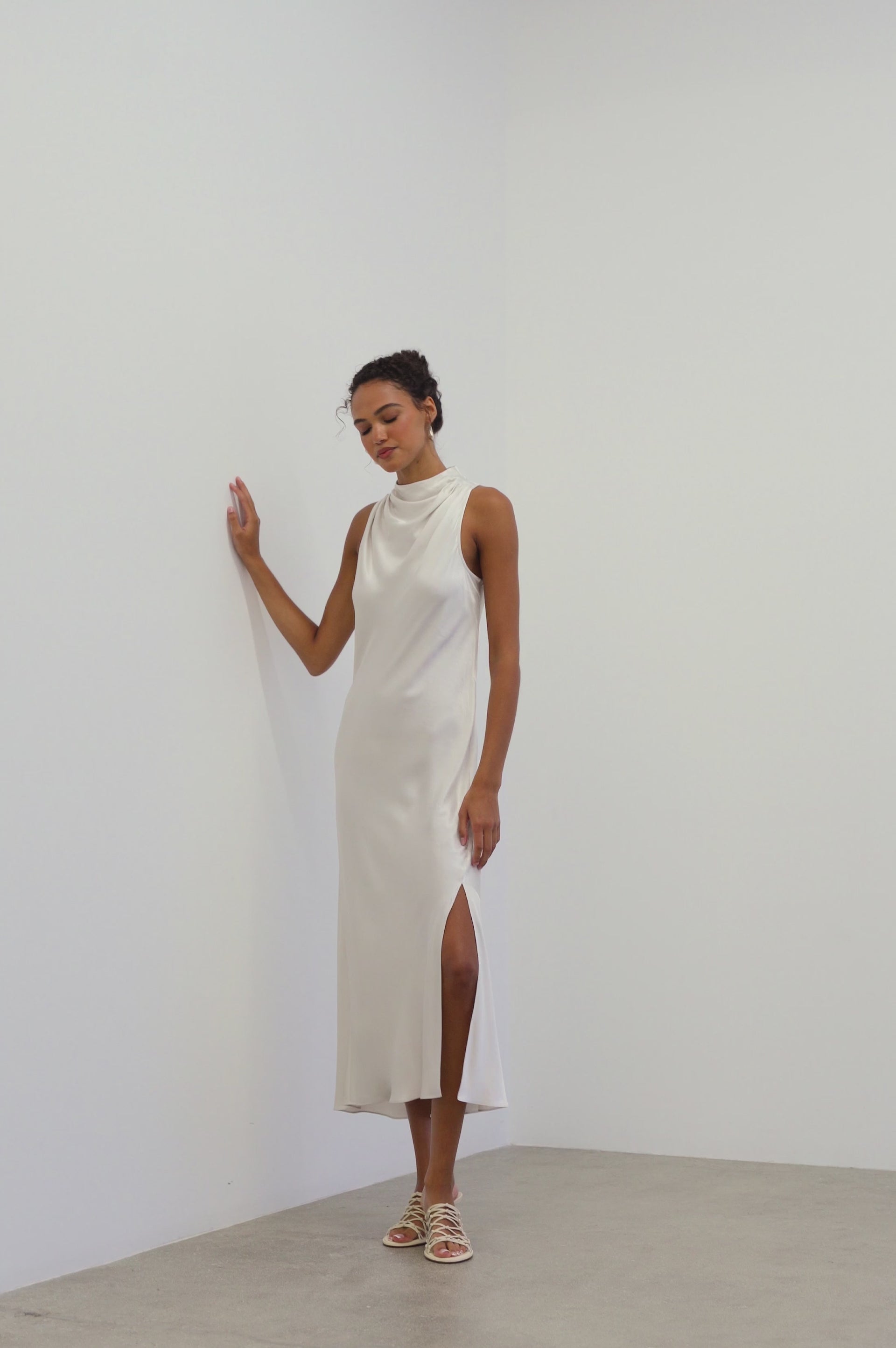 Model wearing the Solana Dress in Ivory, a midi length dress with a side sliit