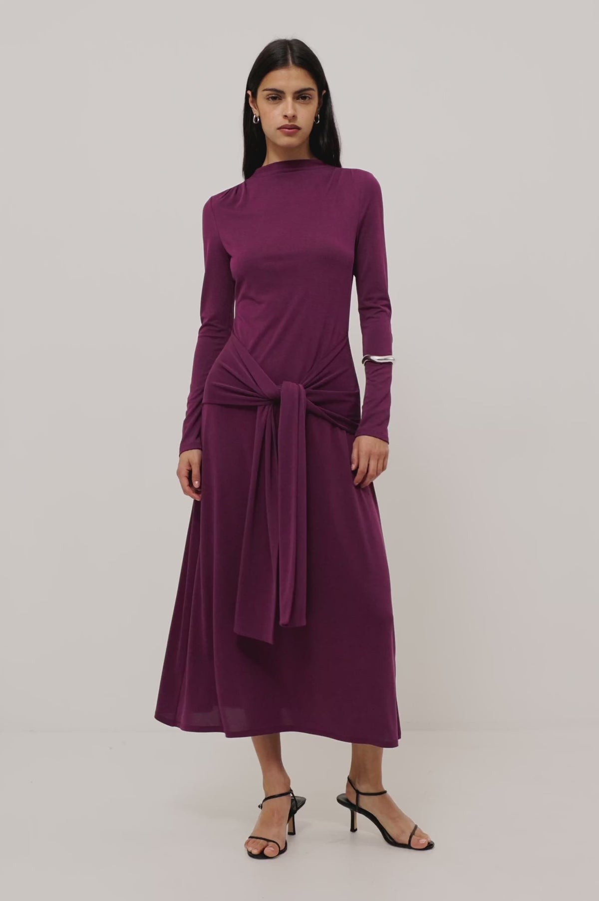 Hollis Midi Dress in Soft Jersey With Mockneck, Front Waist Ties, Pleated Shoulders, Long Sleeves, and A-Line Skirt in Wine Colorway - Full Body View Featured on Model Moving (Video).