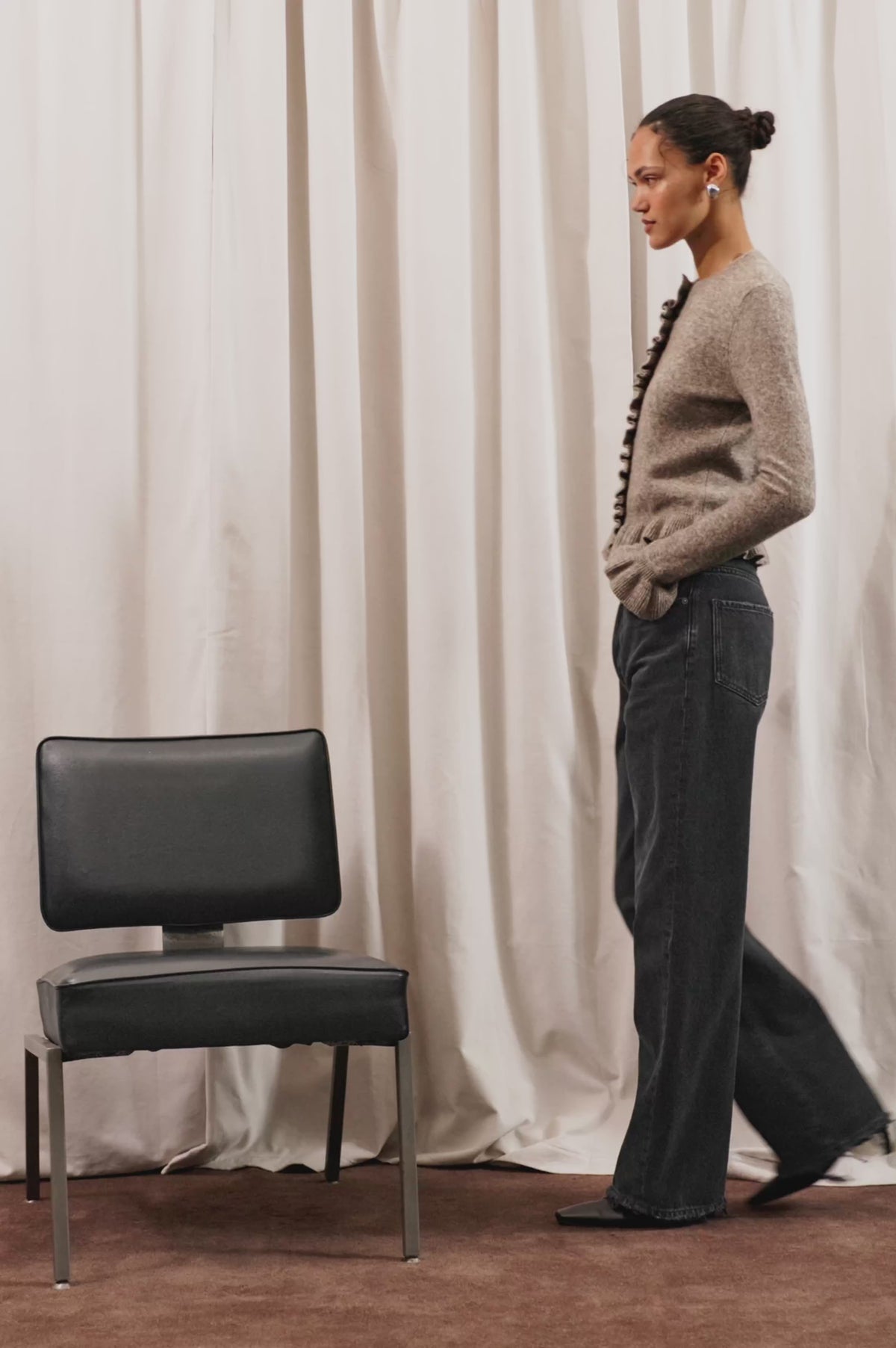 Mandy Sweater in Cashmere-Cotton-Wool Blend Knit Front Buttons, Long Sleeves, Classic Slightly Cropped Fit, and Ribbed Ruffle Trim in Heather Latte Colorway - Full Body View Featured on Model Posing with Chair (Video).