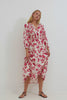 Matia Maxi Dress in Cotton With Banded Ruffle V-Neckline With Self-Ties Elastic Waist and Long Raglan Puff Sleeves in Red Jasmine Colorway - Full Body Front View Featured on Model Sitting - Video