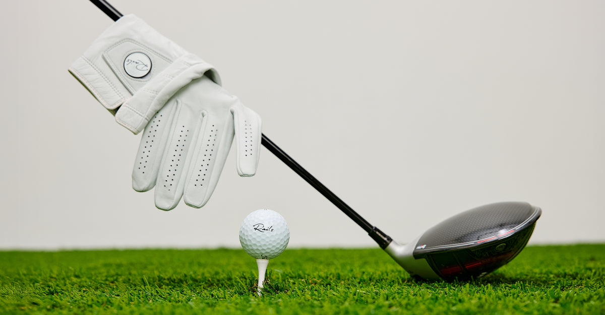 Golf club, golf ball, and glove on a green surface with a white background