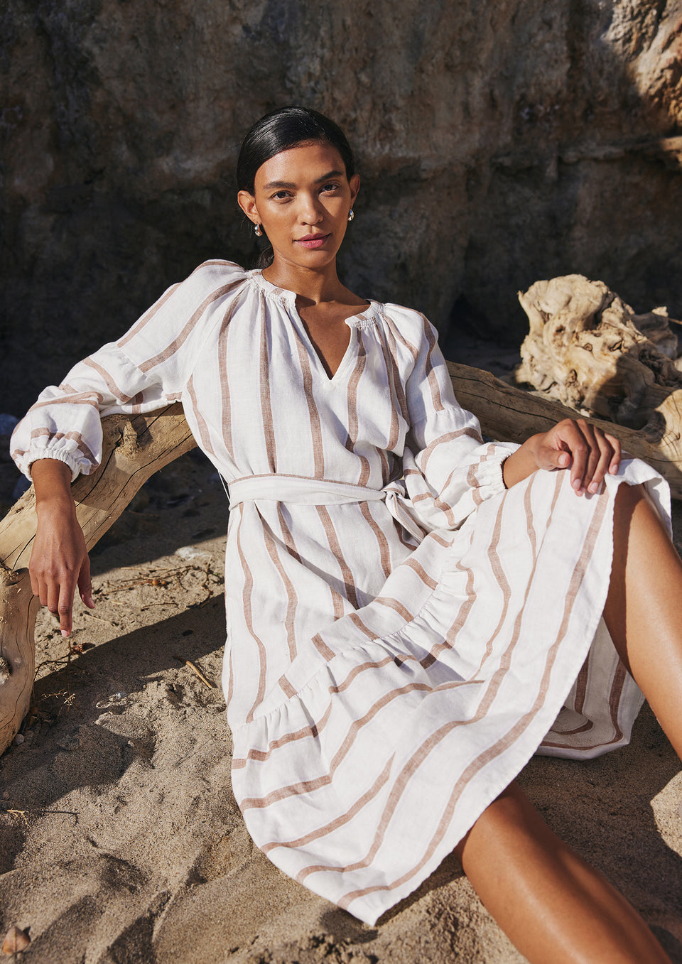 EDITORIAL IMAGE OF MODEL SITTING ON THE BEACH WEARING VITTORIA DRESS IN COCONUT STRIPE