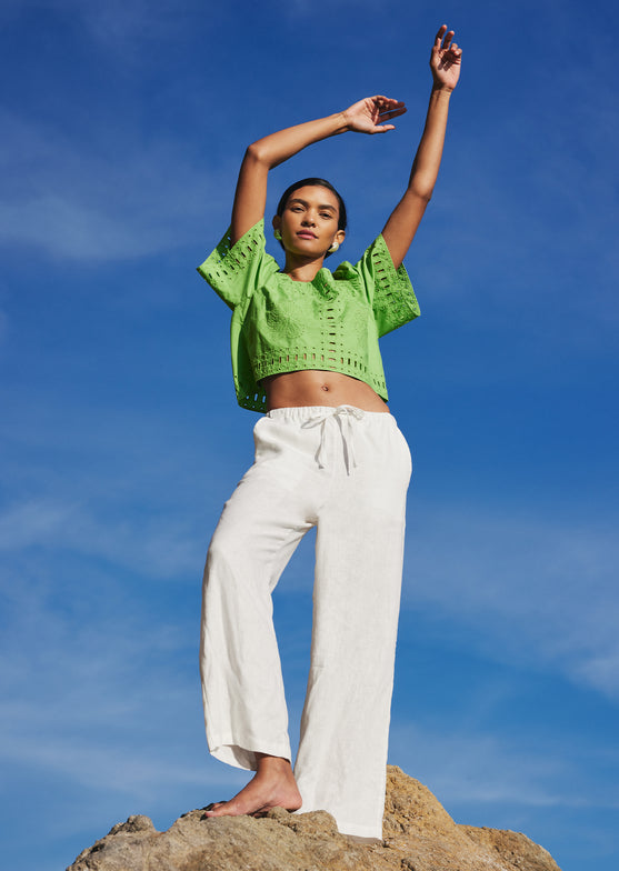 FRONT FULL BODY EDITORIAL IMAGE OF MODEL ON THE BEACH WEARING LAINE TOP IN ISLAND GREEN AND EMMIE PANT IN WHITE