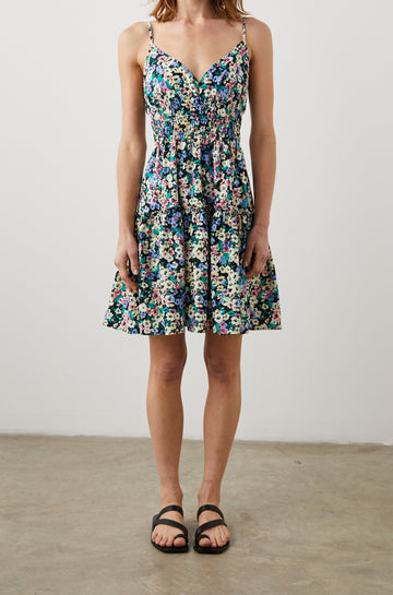 Carmen Sleeveless Mini Dress with Adjustable Spaghetti Straps, a Deep V Neck, a Tiered Skirt and Smocking at the Mid-Bodice in Wildflower Meadow Colorway, Yellow, Purple, Green and Pink on Black - Front Full Body View Featured on Model  