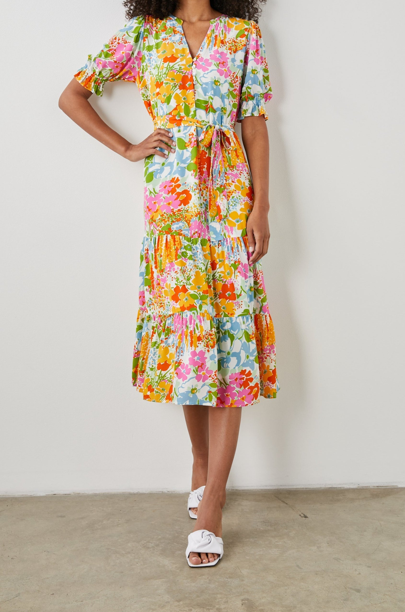 Eliana Midi Dress with Elbow-Length Sleeves with Shirred Cuffs, a V Neck, Buttons Down the Bodice, a Fabric Tie at the Waist  and a Tiered Skirt in Day Garden Colorway, a Floral Pattern in Blue, Pink and Oranges on White - Front Full Body View Featured on Model