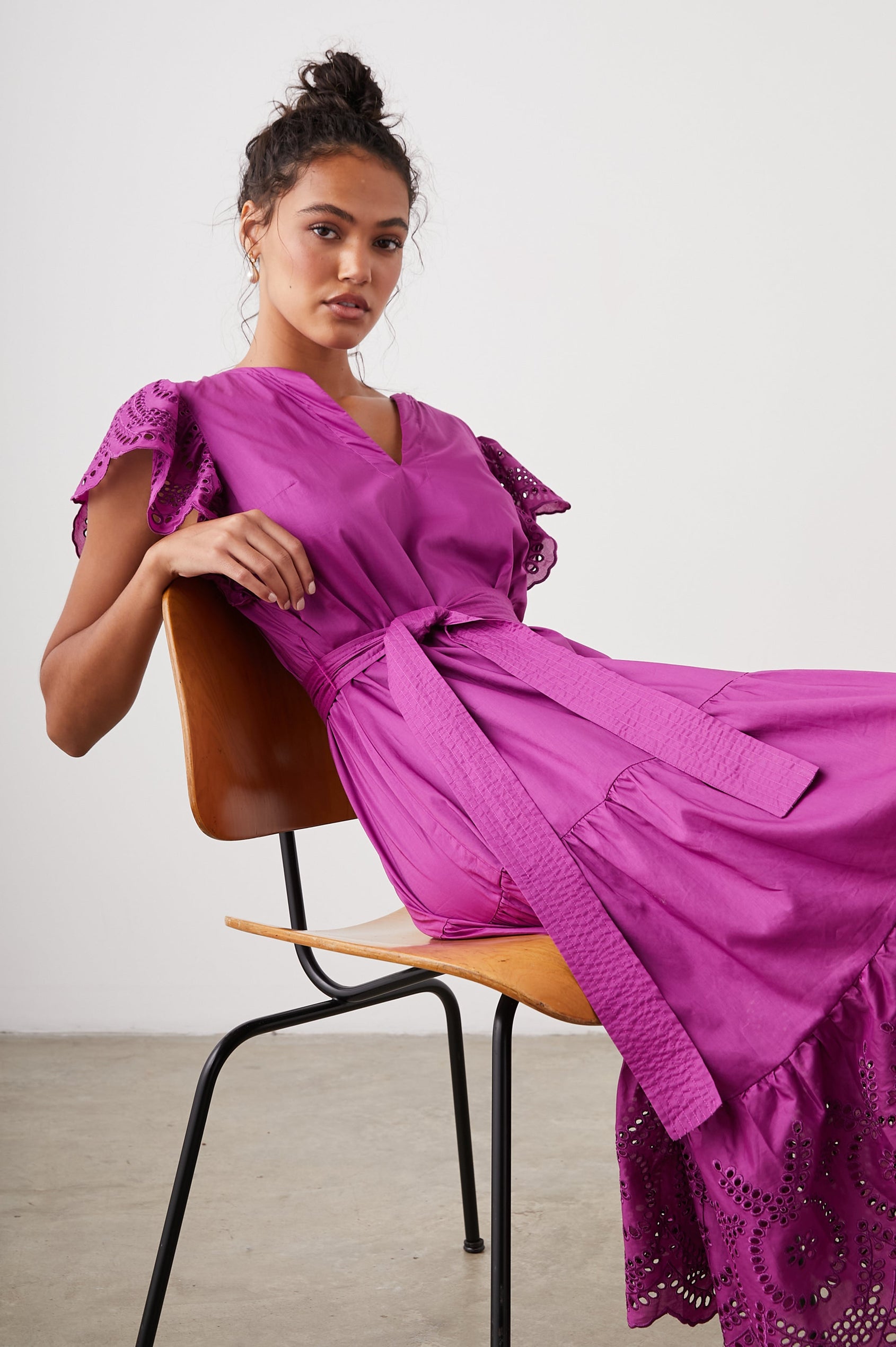 Gia Short-Sleeve Midi Dress with Flutter Sleeves, a V Neck, a Fabric Tie at the Waist, a Tiered Skirt and Eyelet Detail on the Sleeves and Hem in Berry Colorway - Front Full Body View Featured on Seated Model