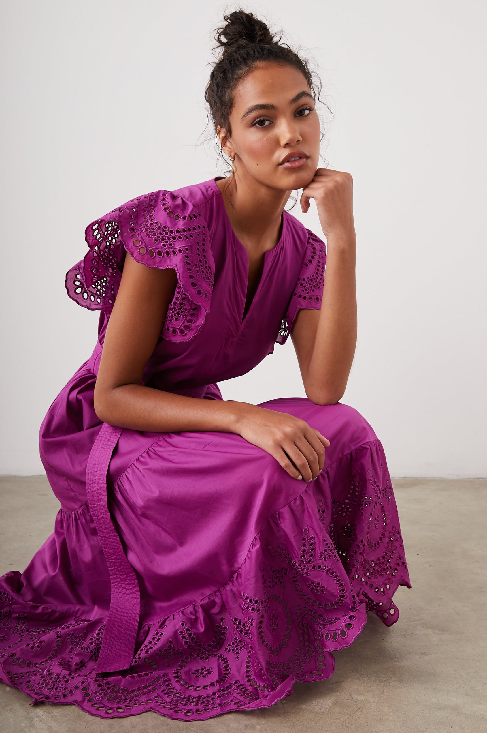 Gia Short-Sleeve Midi Dress with Flutter Sleeves, a V Neck, a Fabric Tie at the Waist, a Tiered Skirt and Eyelet Detail on the Sleeves and Hem in Berry Colorway - Front Full Body View Featured on Seated Model