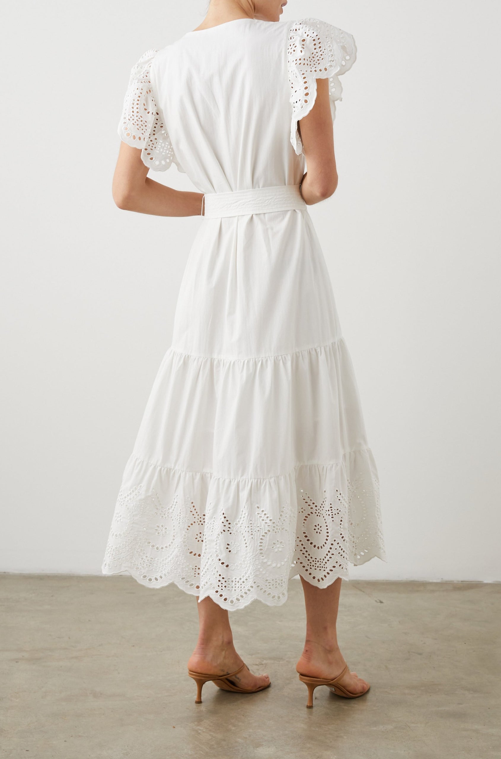Gia Short-Sleeve Midi Dress with Flutter Sleeves, a V Neck, a Fabric Tie at the Waist, a Tiered Skirt and Eyelet Detail on the Sleeves and Hem in White Colorway - Back Full Body View Featured on Model