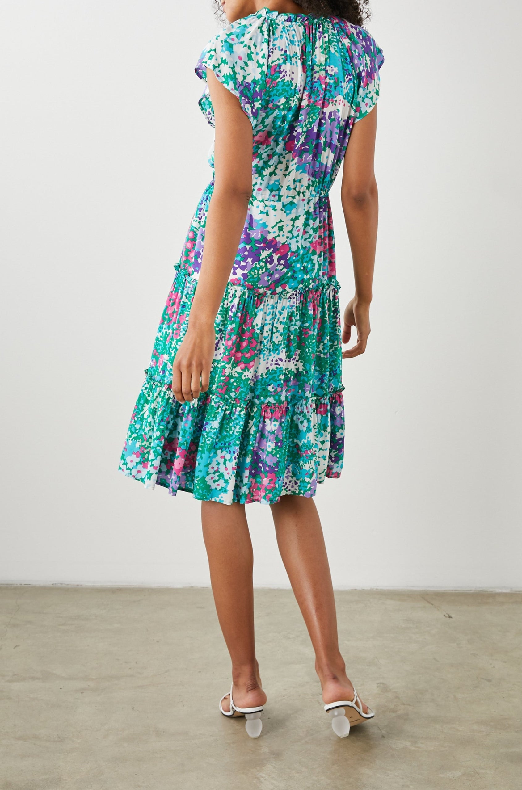 Juni Short Sleeve Midi Dress with a V Neck, Light Ruching along the Neckline, a Drawstring Waist, and a Tiered Skirt in Gardenia Floral Colorway, in Greens, Blues, Purples, Pinks and White - Back Full Body View Featured on Model
